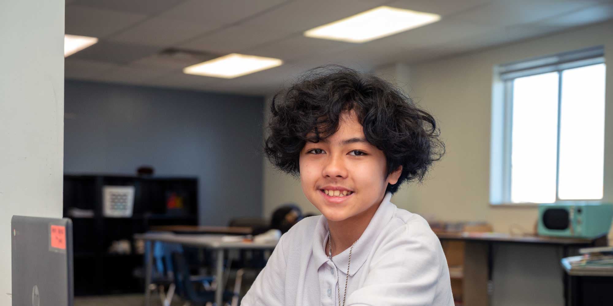 Smiling student with curly hair in a classroom.